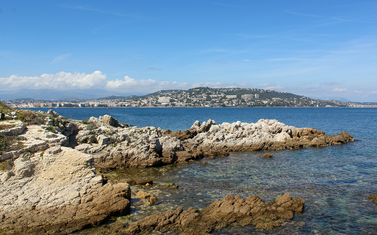 Rocky coastline of Ste. Marguerite Island with Cannes in the background across the sea.