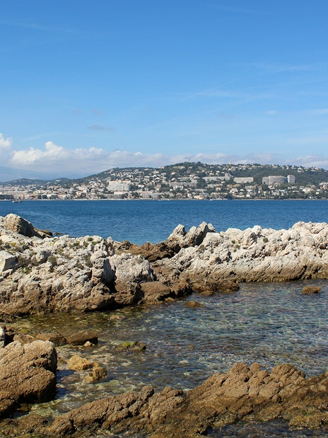 Rocky coastline of Ste. Marguerite Island with Cannes in the background across the sea.
