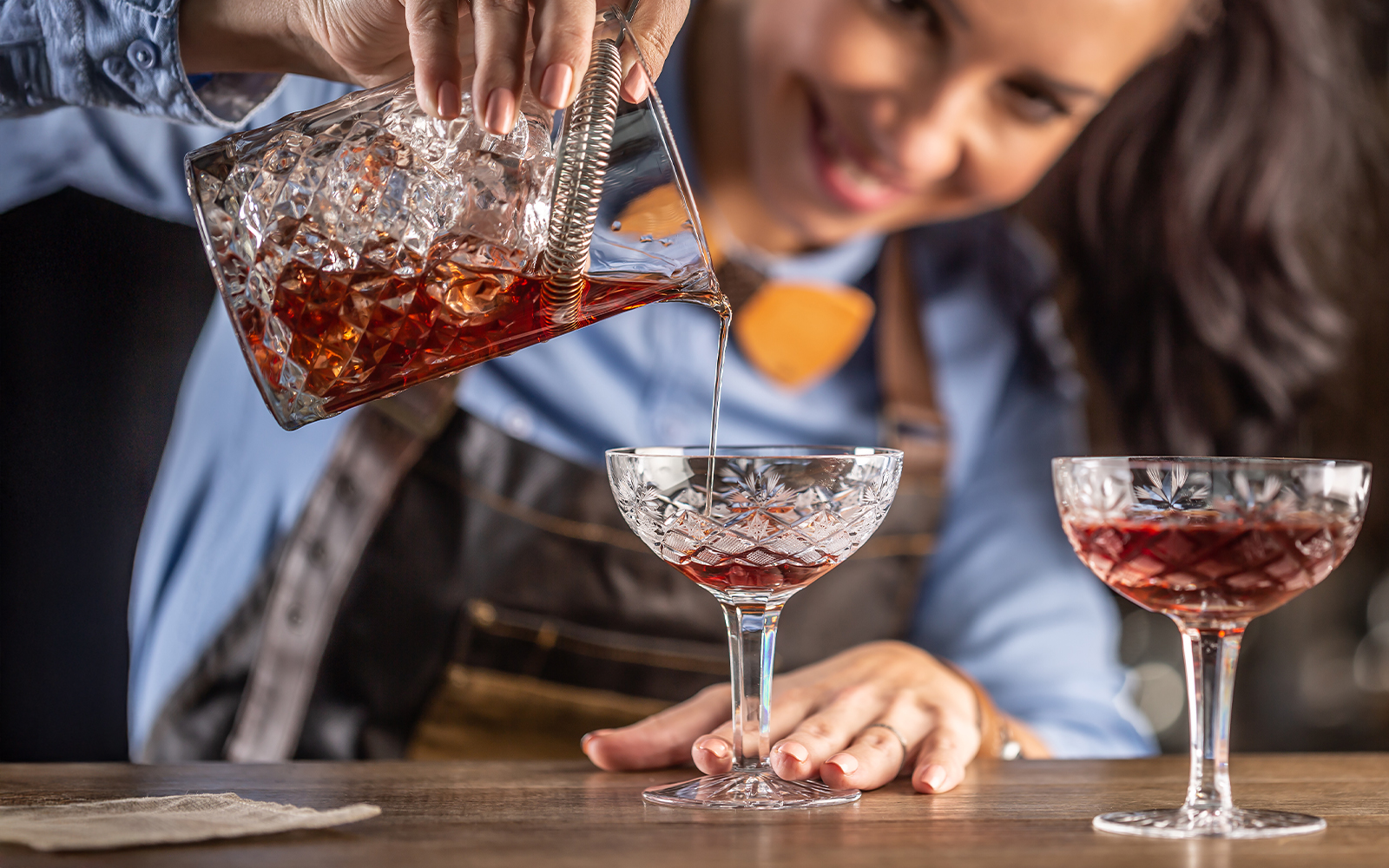 Bartender pouring vermouth cocktail into a crystal glass.