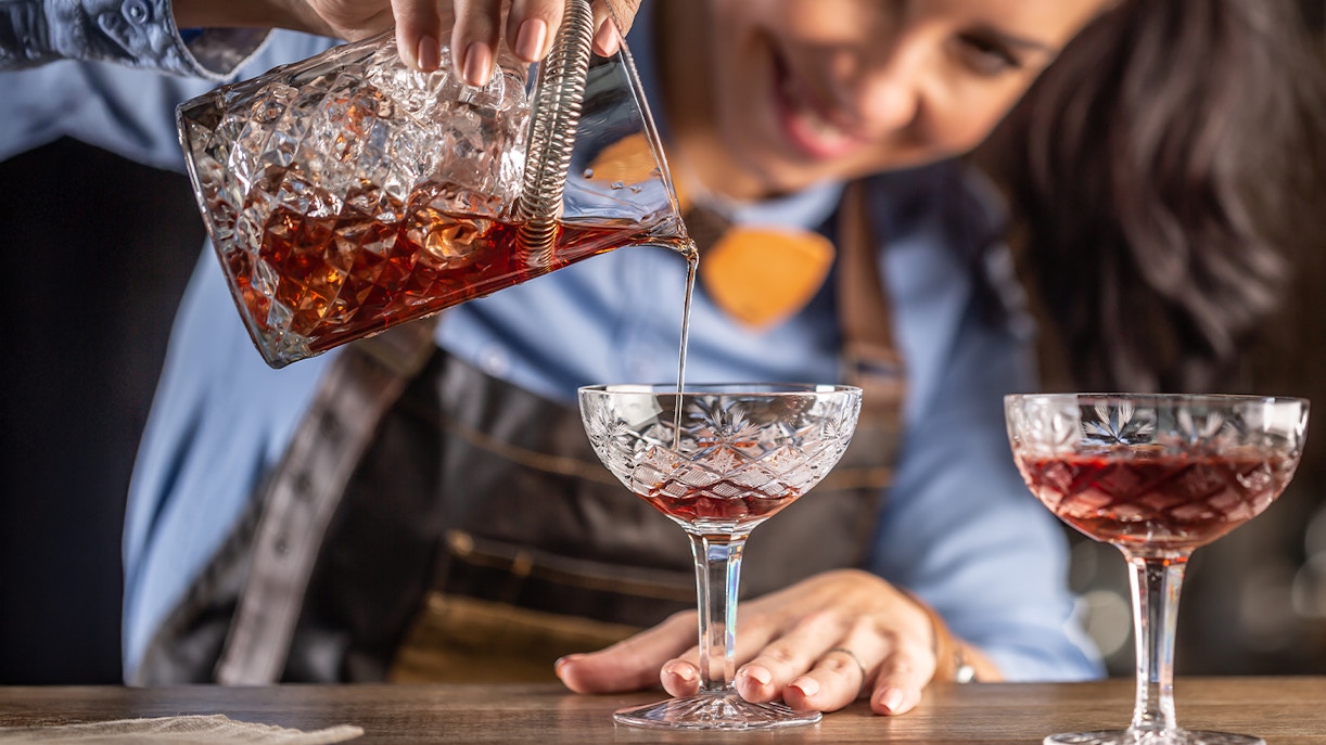Bartender pouring vermouth cocktail into a crystal glass.