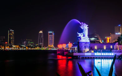 Da Nang Dragon Bridge lit at night with city skyline in background.