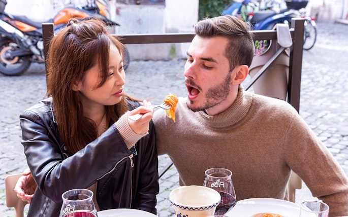 Couple sharing pasta at an outdoor Italian cafe.
