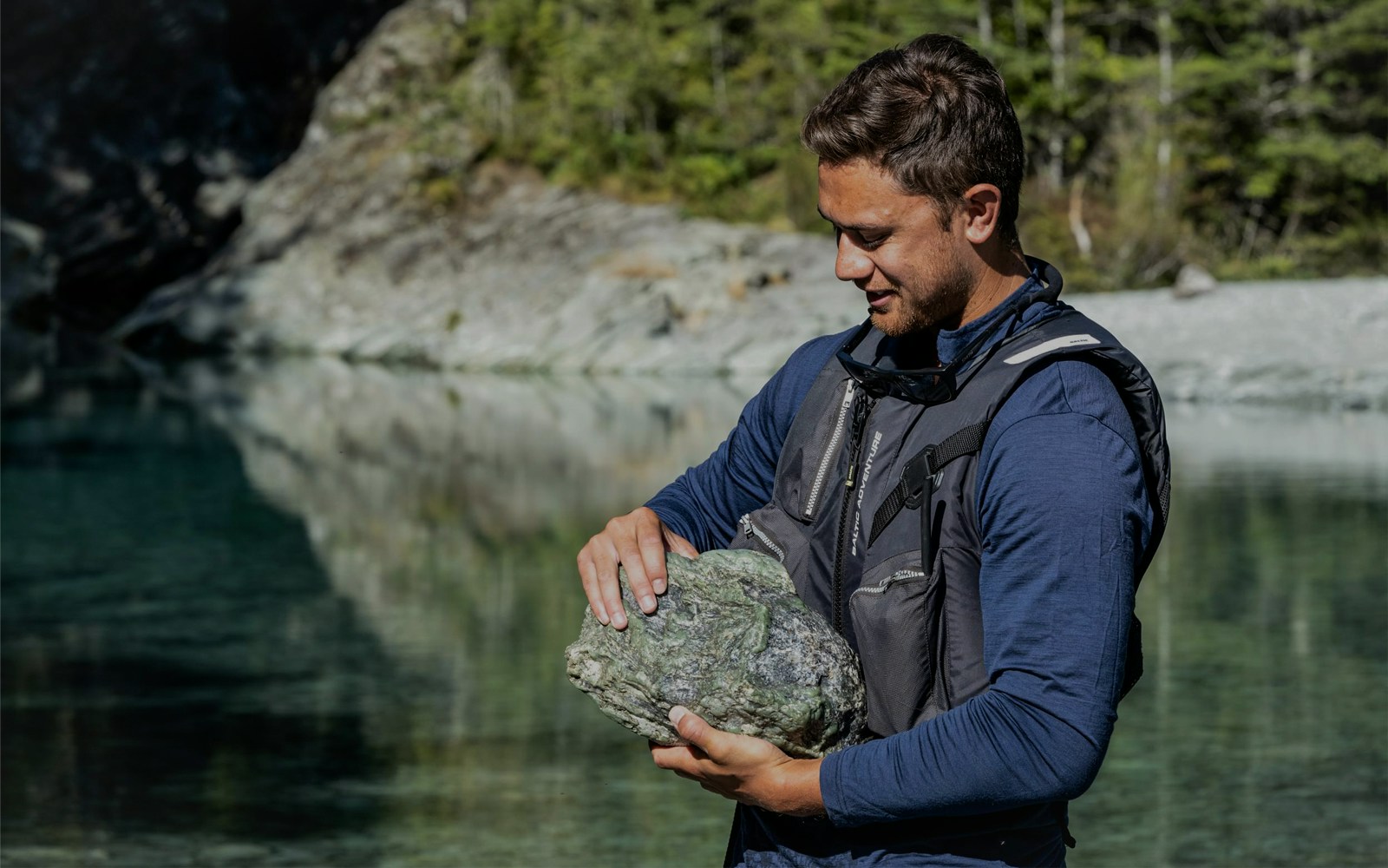 Man holding a large rock by the Dart River during a Funyak tour in New Zealand.
