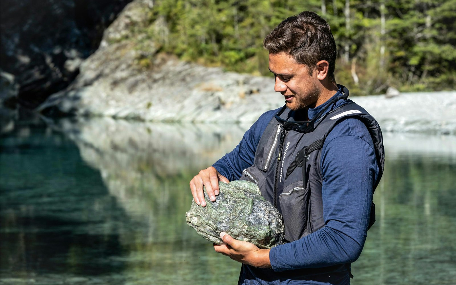 Man holding a large rock by the Dart River during a Funyak tour in New Zealand.