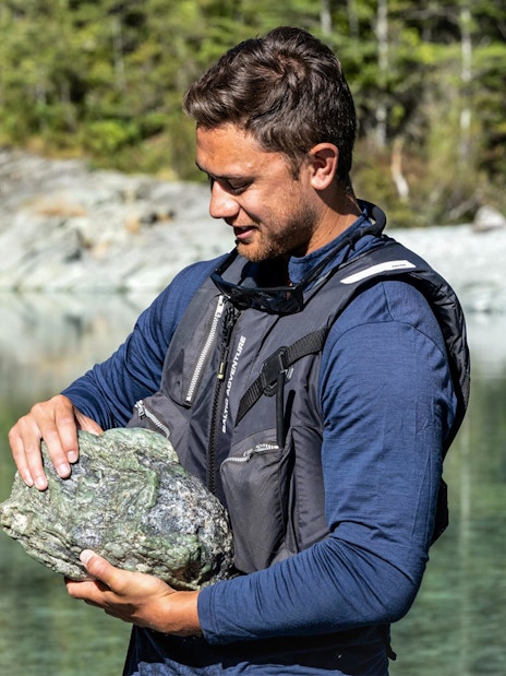Man holding a large rock by the Dart River during a Funyak tour in New Zealand.