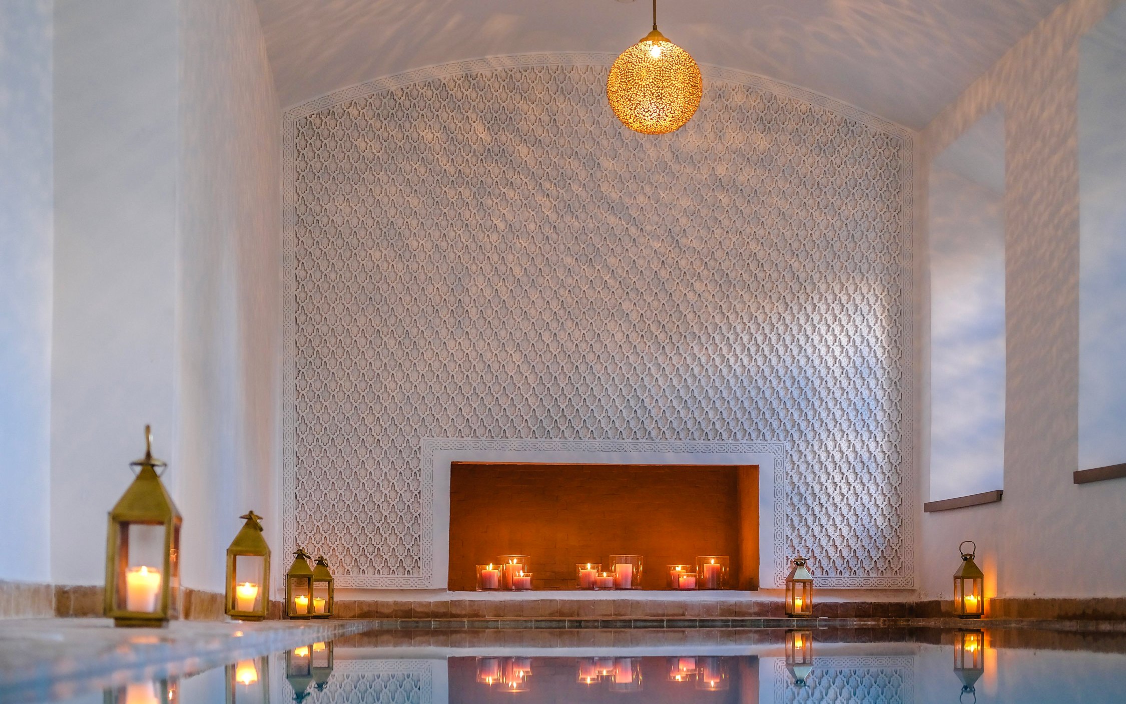 Luxurious steam hammam with ornate walls, candles, and lanterns reflecting on water.