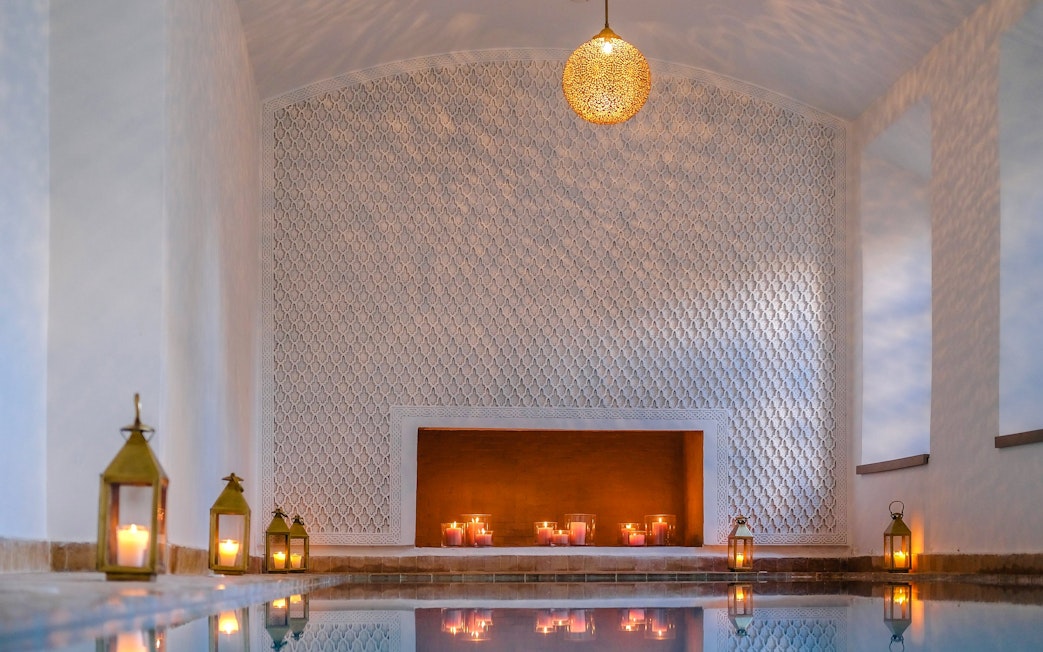 Luxurious steam hammam with ornate walls, candles, and lanterns reflecting on water.