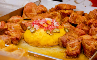 Traditional Romanian Tocana stew with pork, sausages, polenta, and pickles on a metal tray.