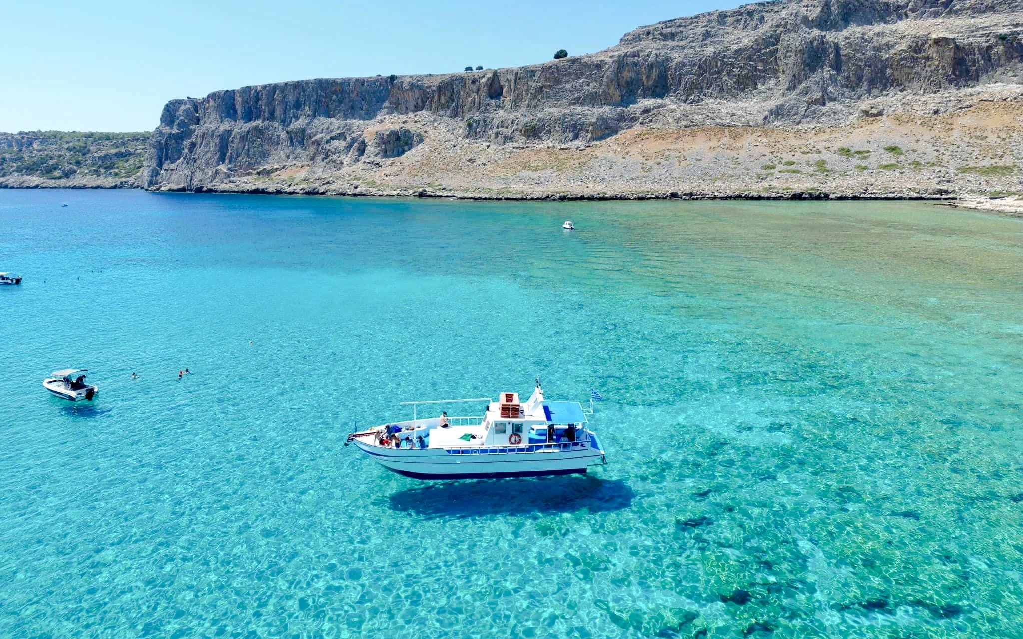 Boat cruising on turquoise sea near Lindos cliffs, Greece.