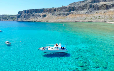 Boat cruising on turquoise sea near Lindos cliffs, Greece.
