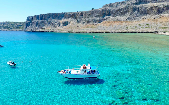 Boat cruising on turquoise sea near Lindos cliffs, Greece.