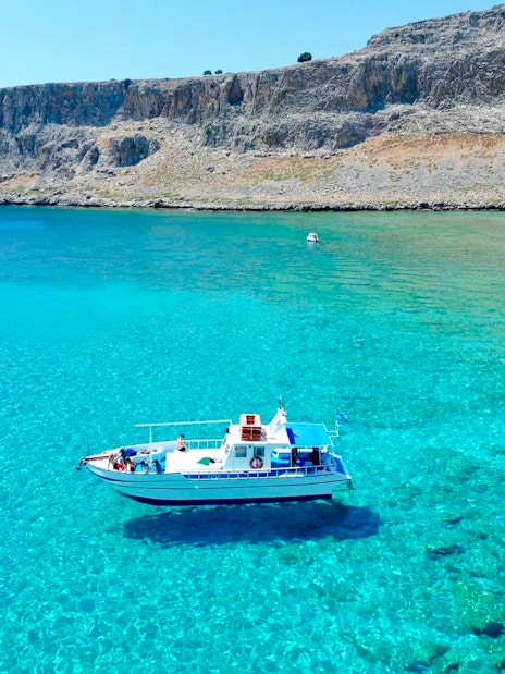 Boat cruising on turquoise sea near Lindos cliffs, Greece.