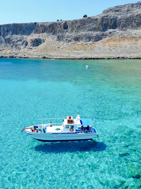 Boat cruising on turquoise sea near Lindos cliffs, Greece.