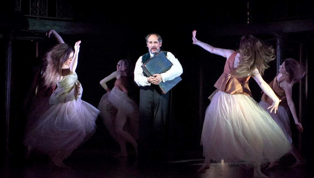 Man holding a book surrounded by dancers in a theatrical performance of Dr Semmelweis.
