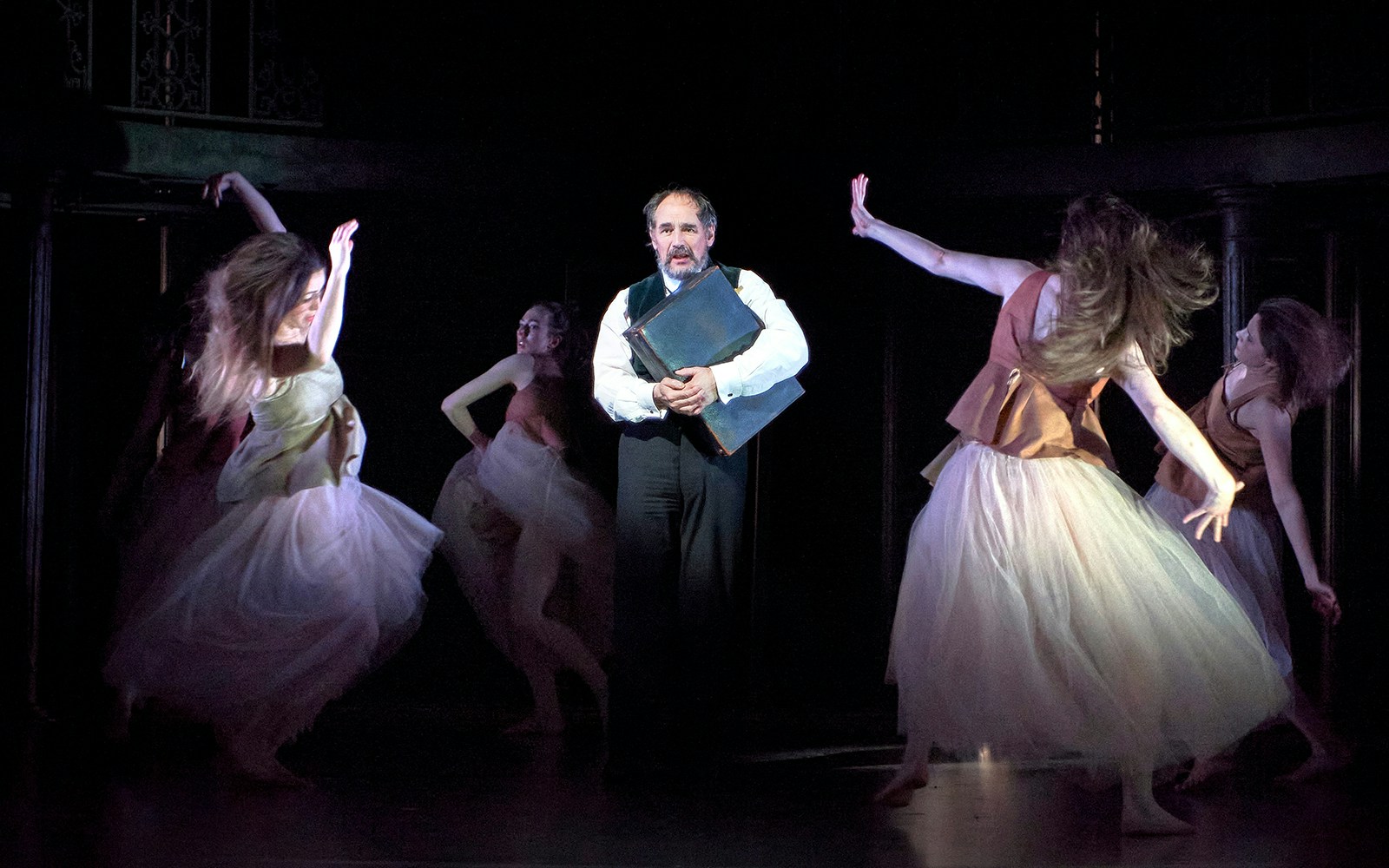 Man holding a book surrounded by dancers in a theatrical performance of Dr Semmelweis.
