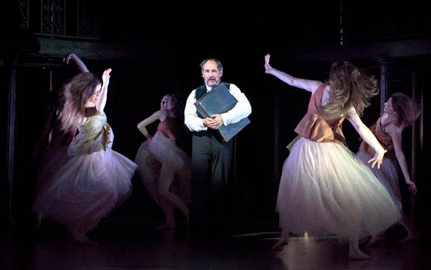 Man holding a book surrounded by dancers in a theatrical performance of Dr Semmelweis.