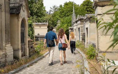 Visitors walking through Père Lachaise Cemetery, Paris, surrounded by historic tombs.
