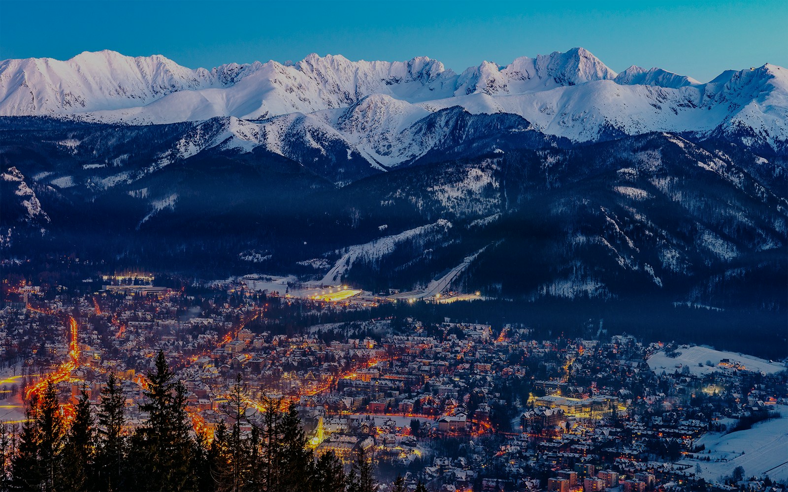 Zakopane cityscape with illuminated streets and snow-covered Tatra Mountains in the background.