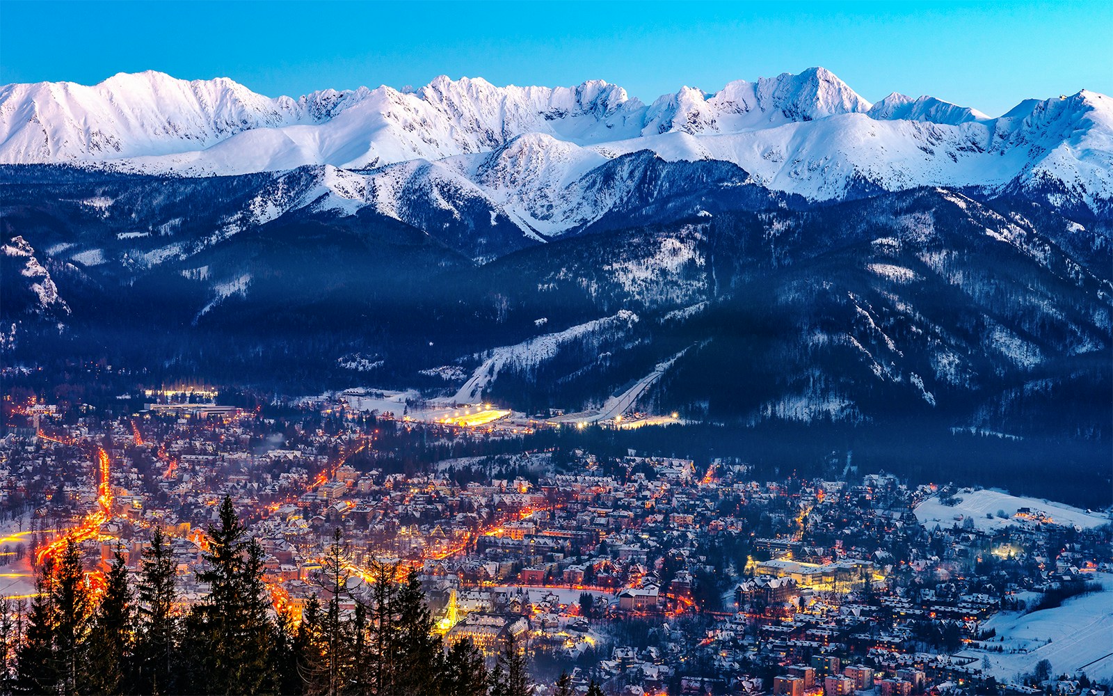 Zakopane cityscape with illuminated streets and snow-covered Tatra Mountains in the background.