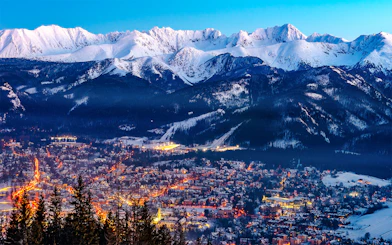 Zakopane cityscape with illuminated streets and snow-covered Tatra Mountains in the background.