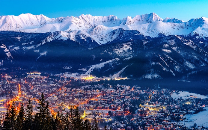 Zakopane cityscape with illuminated streets and snow-covered Tatra Mountains in the background.
