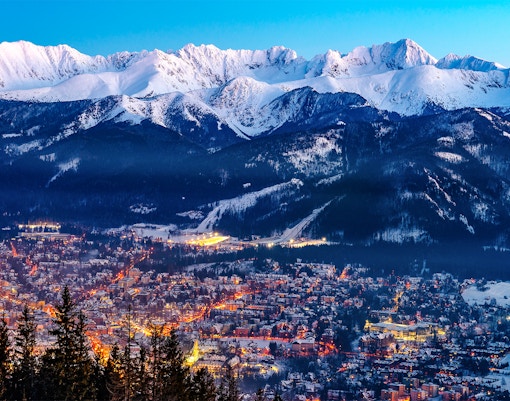Zakopane cityscape with illuminated streets and snow-covered Tatra Mountains in the background.