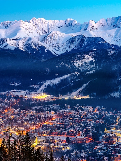 Zakopane cityscape with illuminated streets and snow-covered Tatra Mountains in the background.