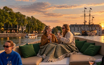 Evening canal cruise in Amsterdam with people enjoying drinks on an open electric boat.