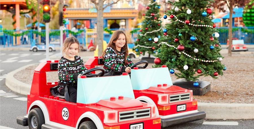Children driving toy cars near decorated Christmas trees at Legoland New York.