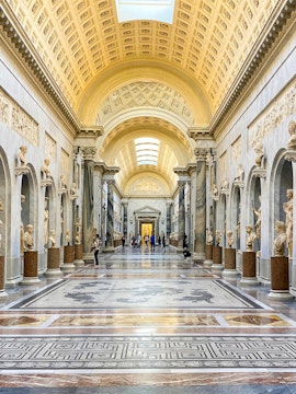 Vatican Museums gallery with ornate ceiling and classical statues, Rome.