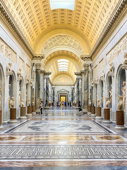 Vatican Museums gallery with ornate ceiling and classical statues, Rome.