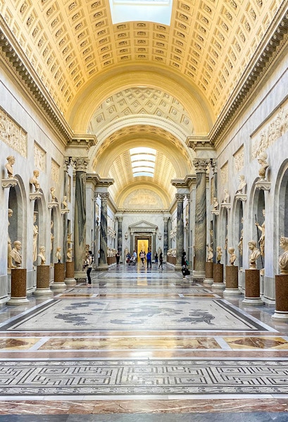 Vatican Museums gallery with ornate ceiling and classical statues, Rome.