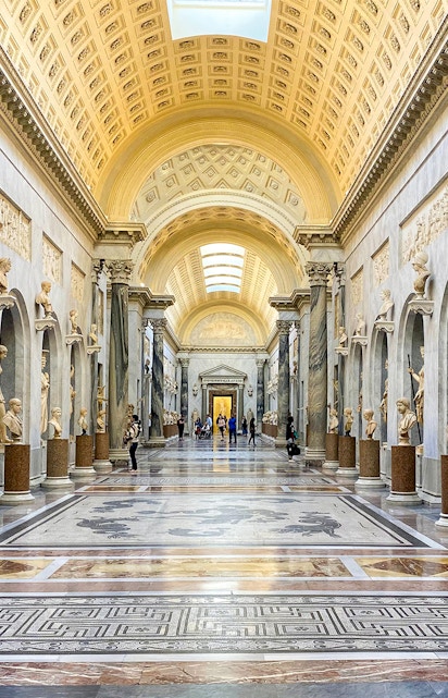 Vatican Museums gallery with ornate ceiling and classical statues, Rome.