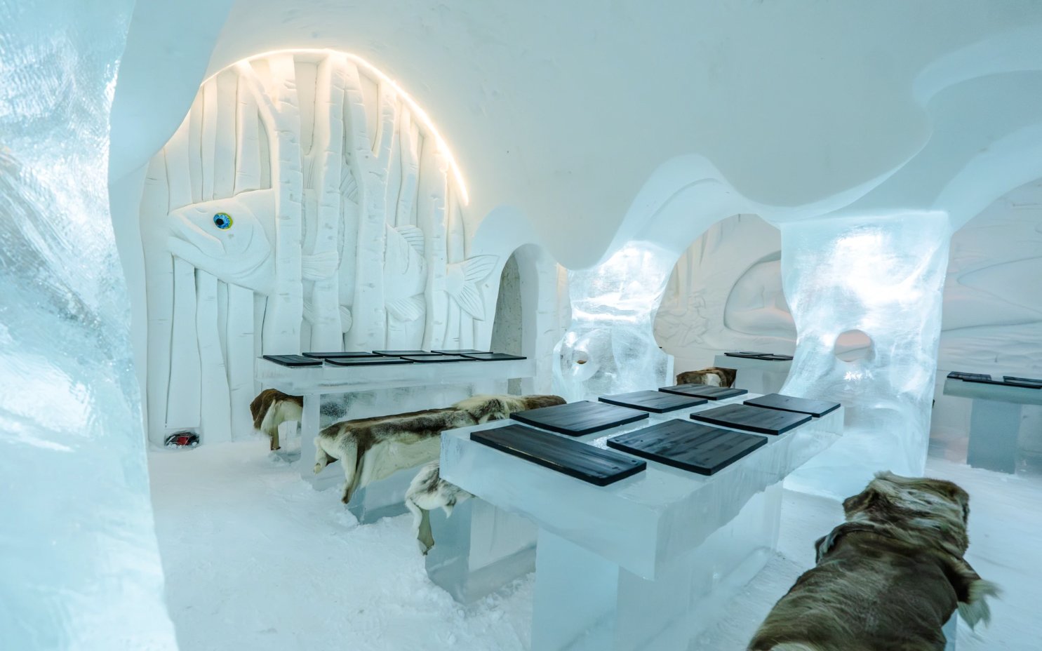 Inside view of Arctic SnowHotel dining area with ice tables and carved fish decor.