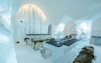 Inside view of Arctic SnowHotel dining area with ice tables and carved fish decor.