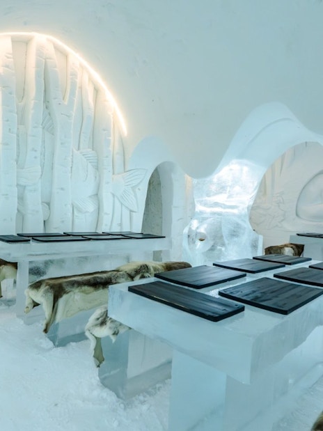 Inside view of Arctic SnowHotel dining area with ice tables and carved fish decor.