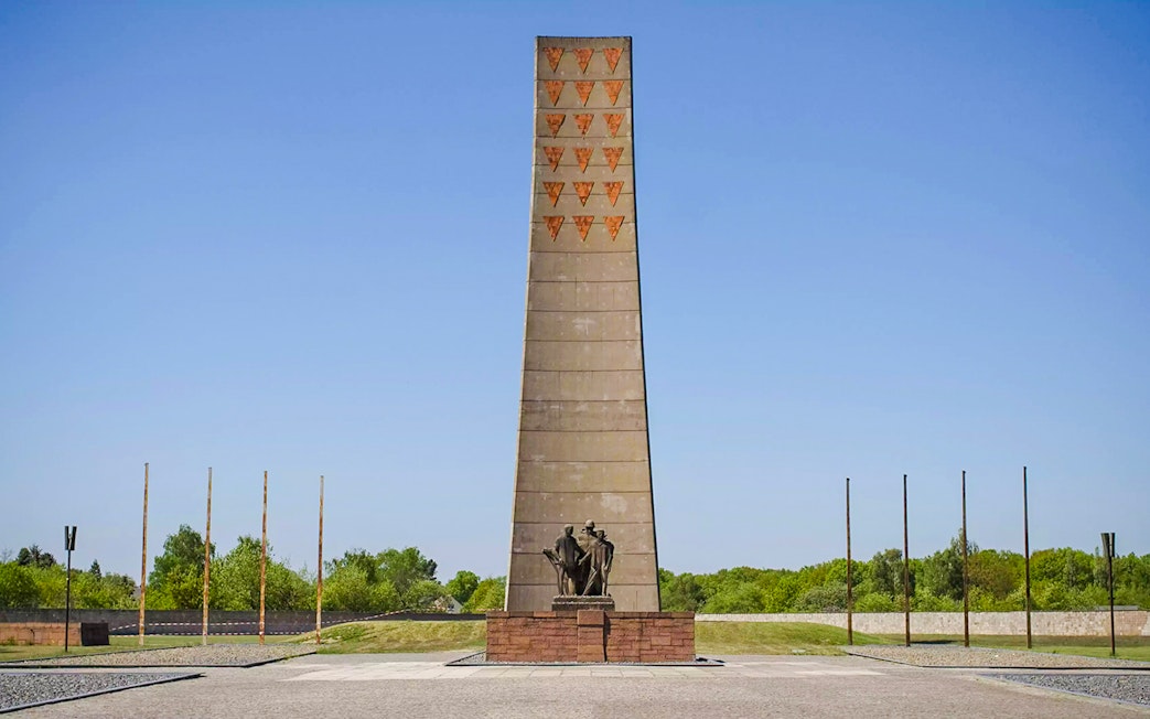 Sachsenhausen Memorial obelisk with statues, surrounded by greenery under a clear sky.