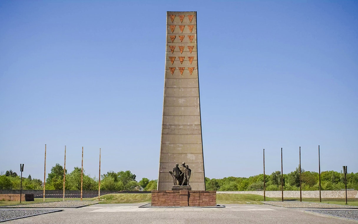 Sachsenhausen Memorial obelisk with statues, surrounded by greenery under a clear sky.