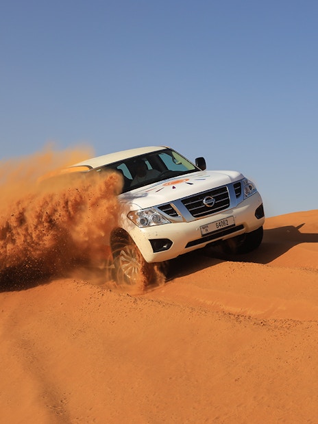 SUV driving through Arabian desert dunes during premium safari experience.