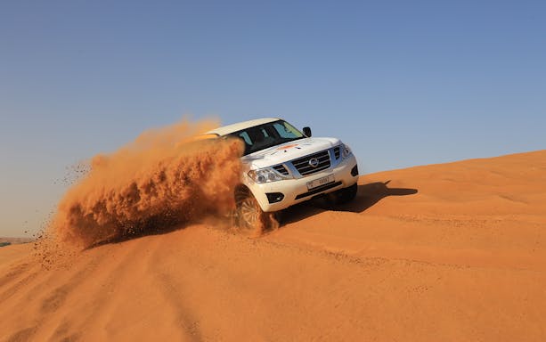 SUV driving through Arabian desert dunes during premium safari experience.