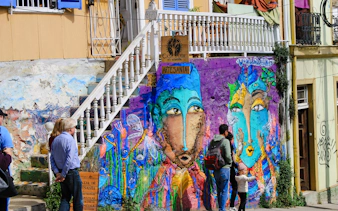 Street art mural in Valparaíso, Chile, with vibrant colors and people observing.