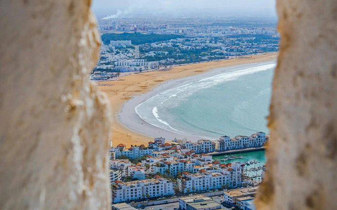 Aerial view of Agadir beach and cityscape framed by ancient walls.