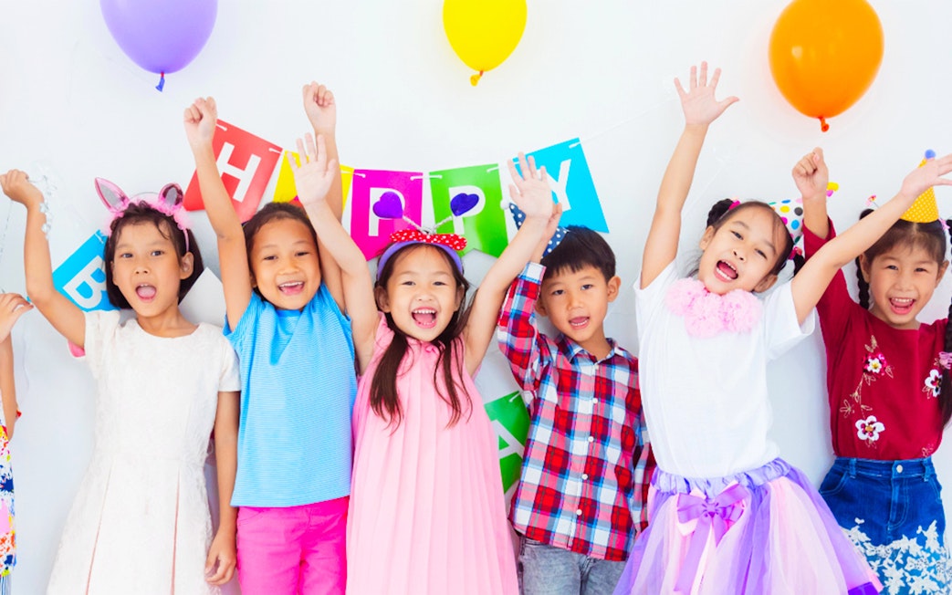 Children celebrating at KidZania with colorful balloons and a birthday banner.