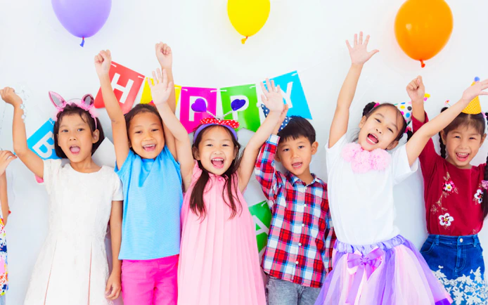 Children celebrating at KidZania with colorful balloons and a birthday banner.