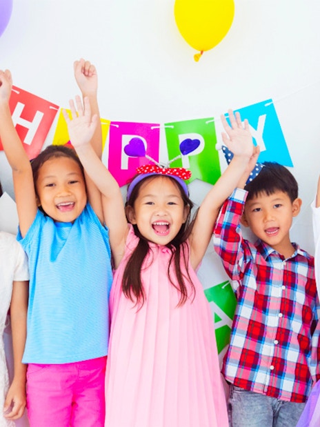 Children celebrating at KidZania with colorful balloons and a birthday banner.