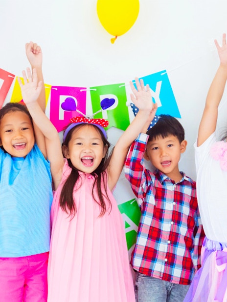 Children celebrating at KidZania with colorful balloons and a birthday banner.