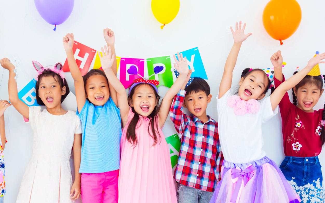 Children celebrating at KidZania with colorful balloons and a birthday banner.