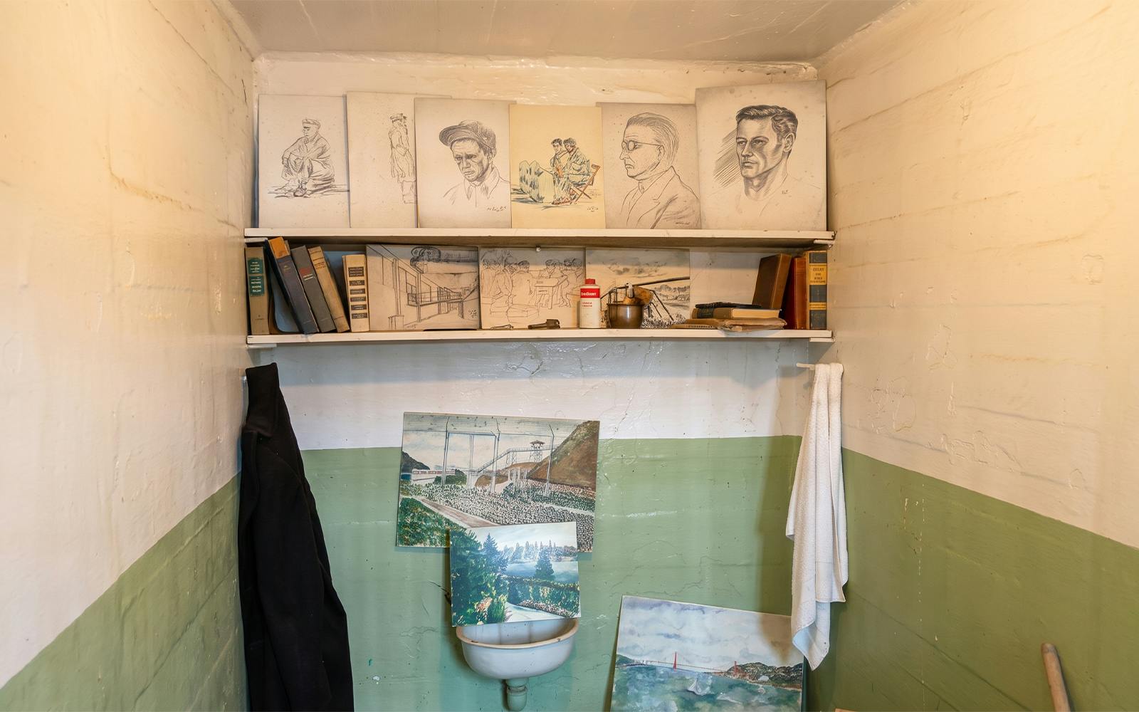 Alcatraz prison cell with inmate artwork and books on shelves.