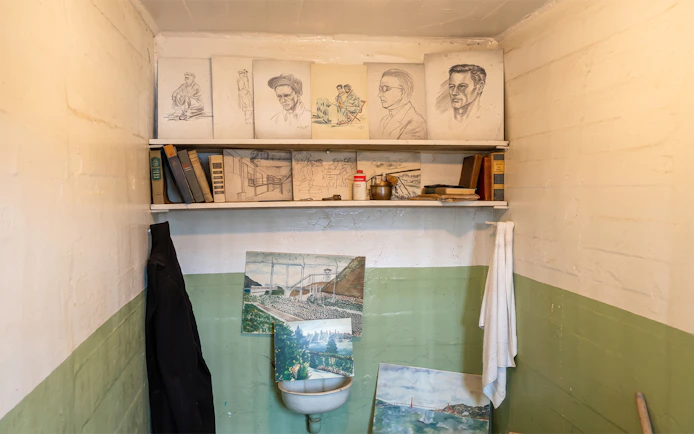 Alcatraz prison cell with inmate artwork and books on shelves.