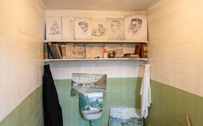 Alcatraz prison cell with inmate artwork and books on shelves.